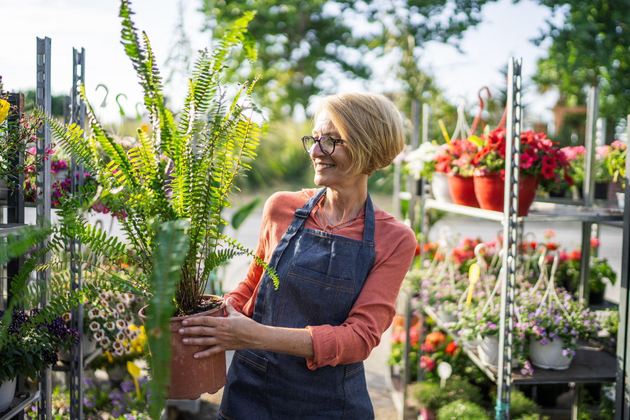 Female florists working alone in garden center outdoors, she is carrying a potted plant.